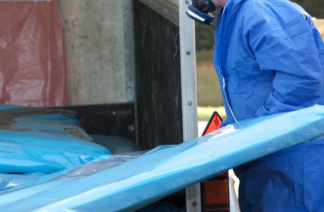 Asbestos corrugated roofing sheet being removed and sealed in a plastic sheet